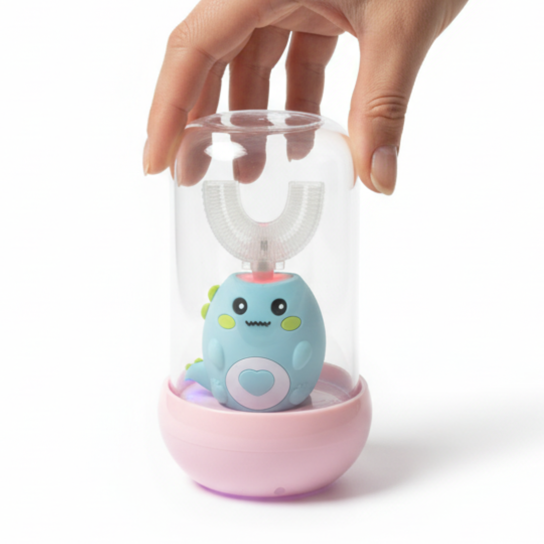 A hand holding a clear cylindrical cover over a small blue cartoon toothbrush device sitting in a pink base, photographed on a clean white background.