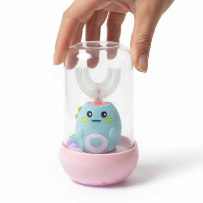 A hand holding a clear cylindrical cover over a small blue cartoon toothbrush device sitting in a pink base, photographed on a clean white background.